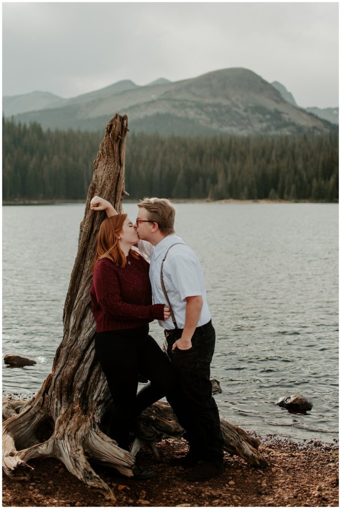 Couple leans up against a dead tree with Brainard Lake in the background