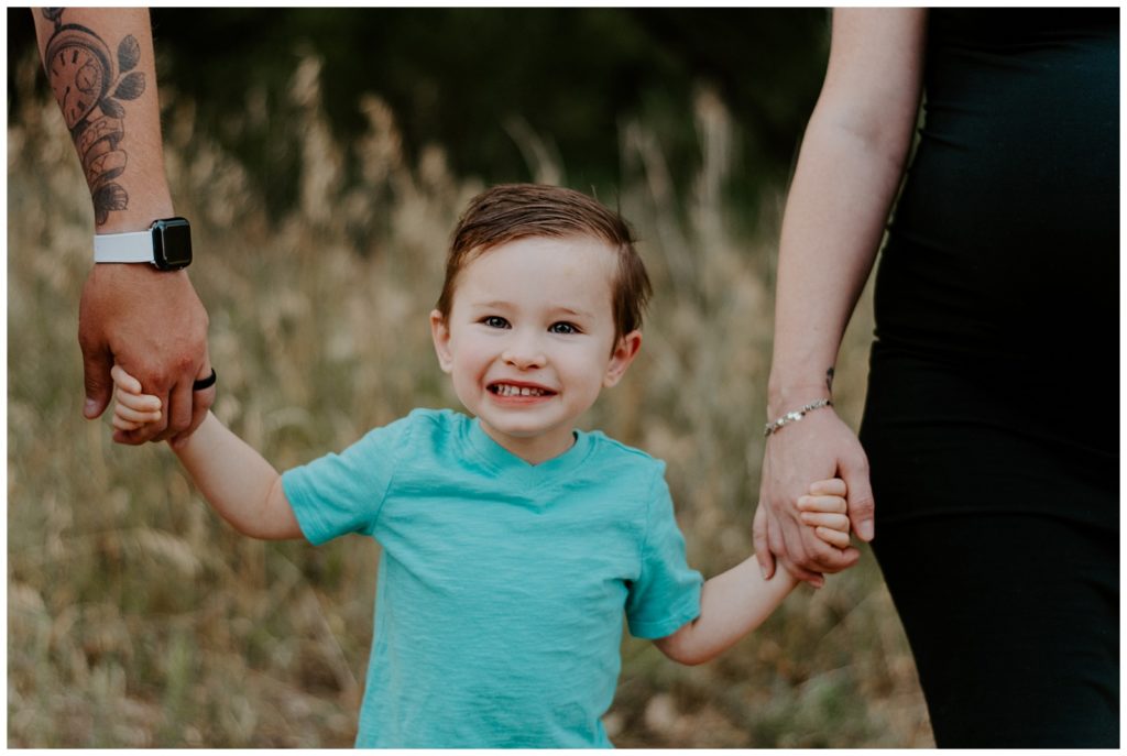 Son smiles while holding mom and dad's hands family session