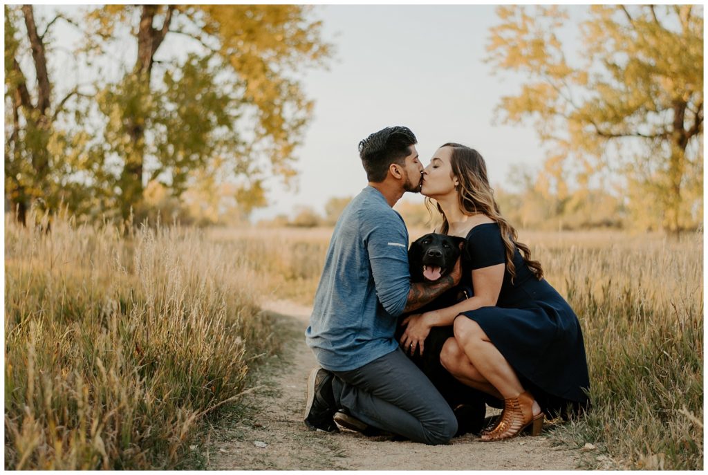 Couple kisses over their black lab at their fall engagement session in Fort Collins