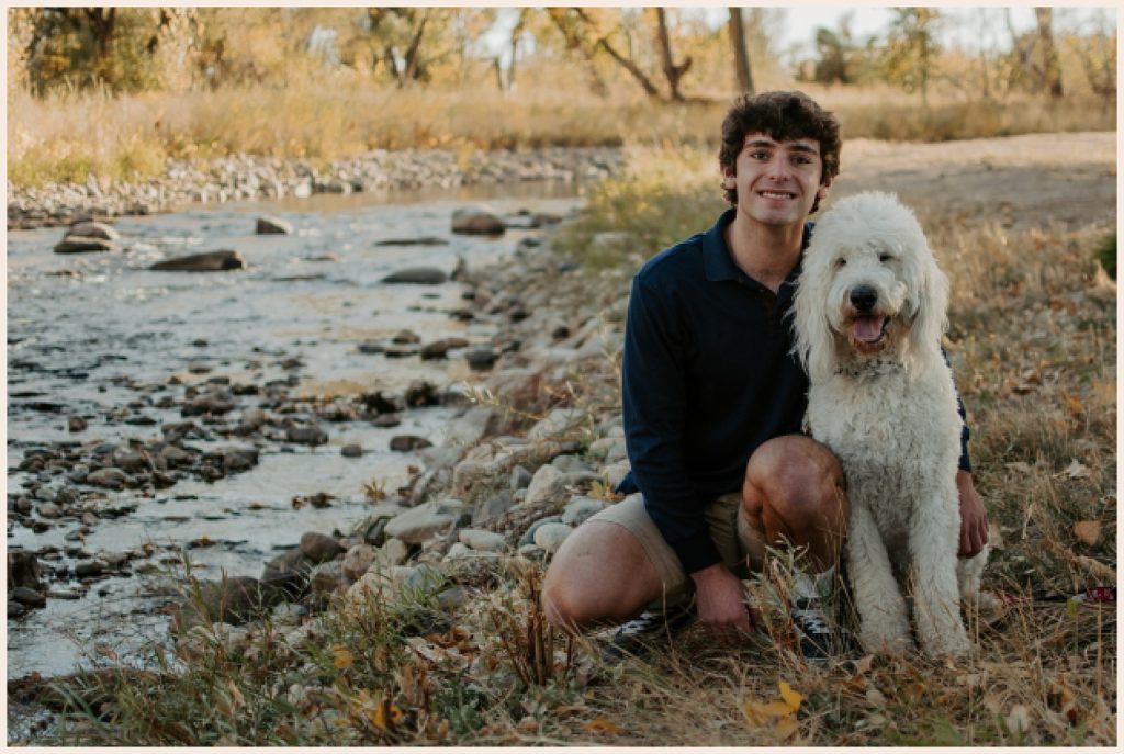 Senior boy sits by the river with his dog