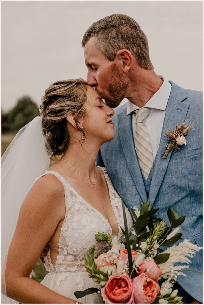 Groom kisses his bride's forehead at Colorado outdoor wedding