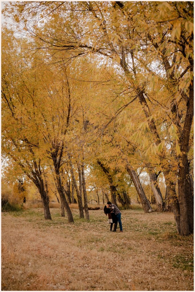 Couple kisses under yellow tress during fall engagement photos in colorado
