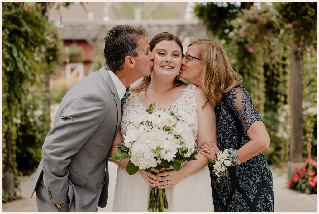 Bride's parents kiss her on the check during Brookside Gardens wedding 
