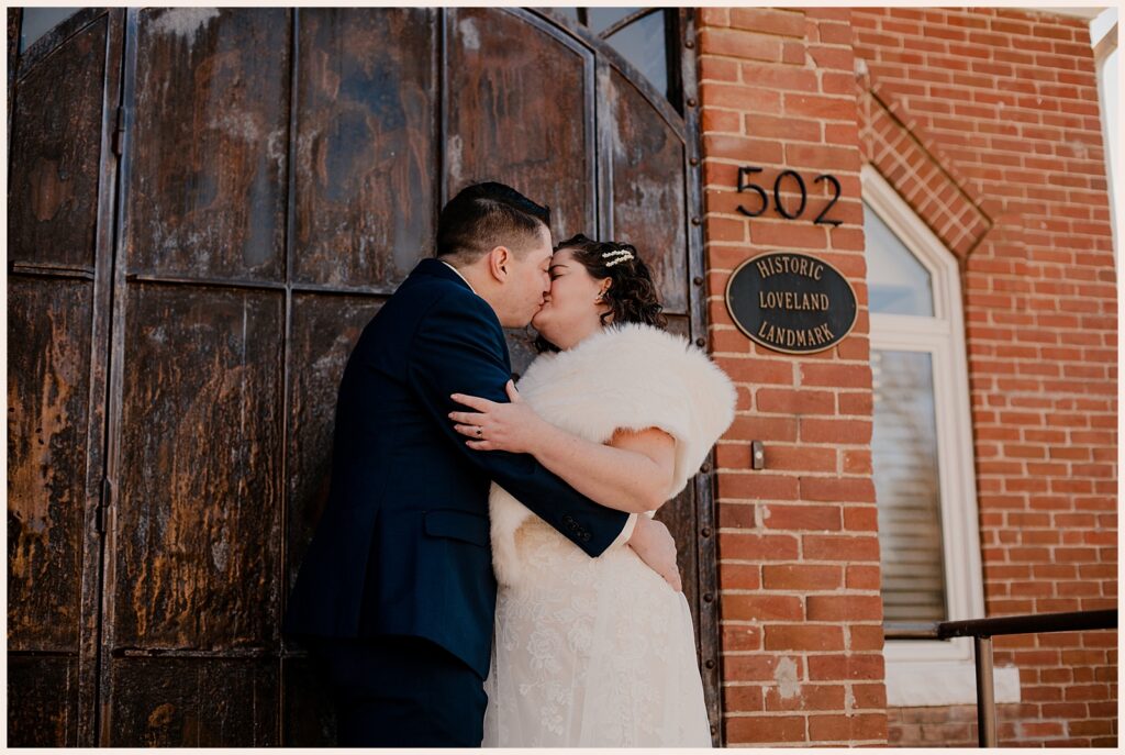 Couple kiss outside wooden doors at Sweetheart Winery wedding 