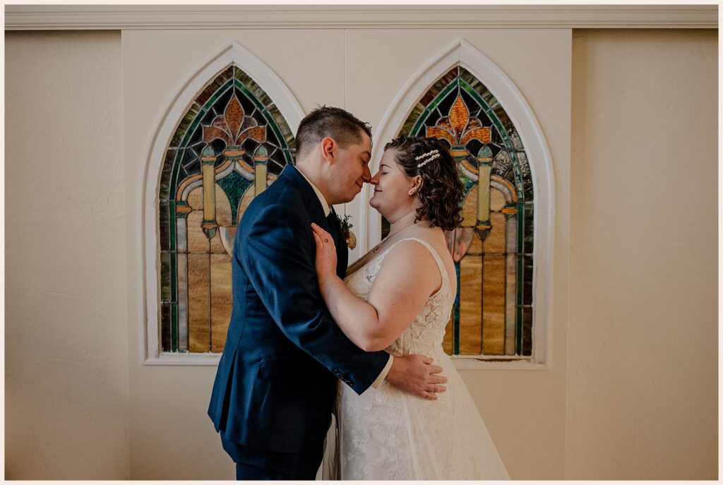 Couple stand nose to nose in front of stained glass during their Sweetheart Winery wedding 