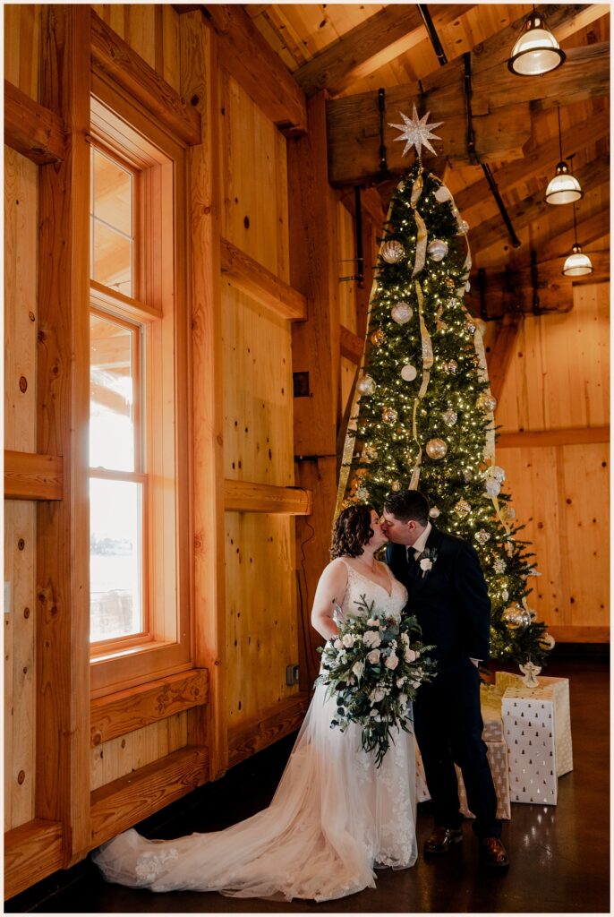 Couple kisses in front of Christmas tree at their Sweetheart Winery Wedding